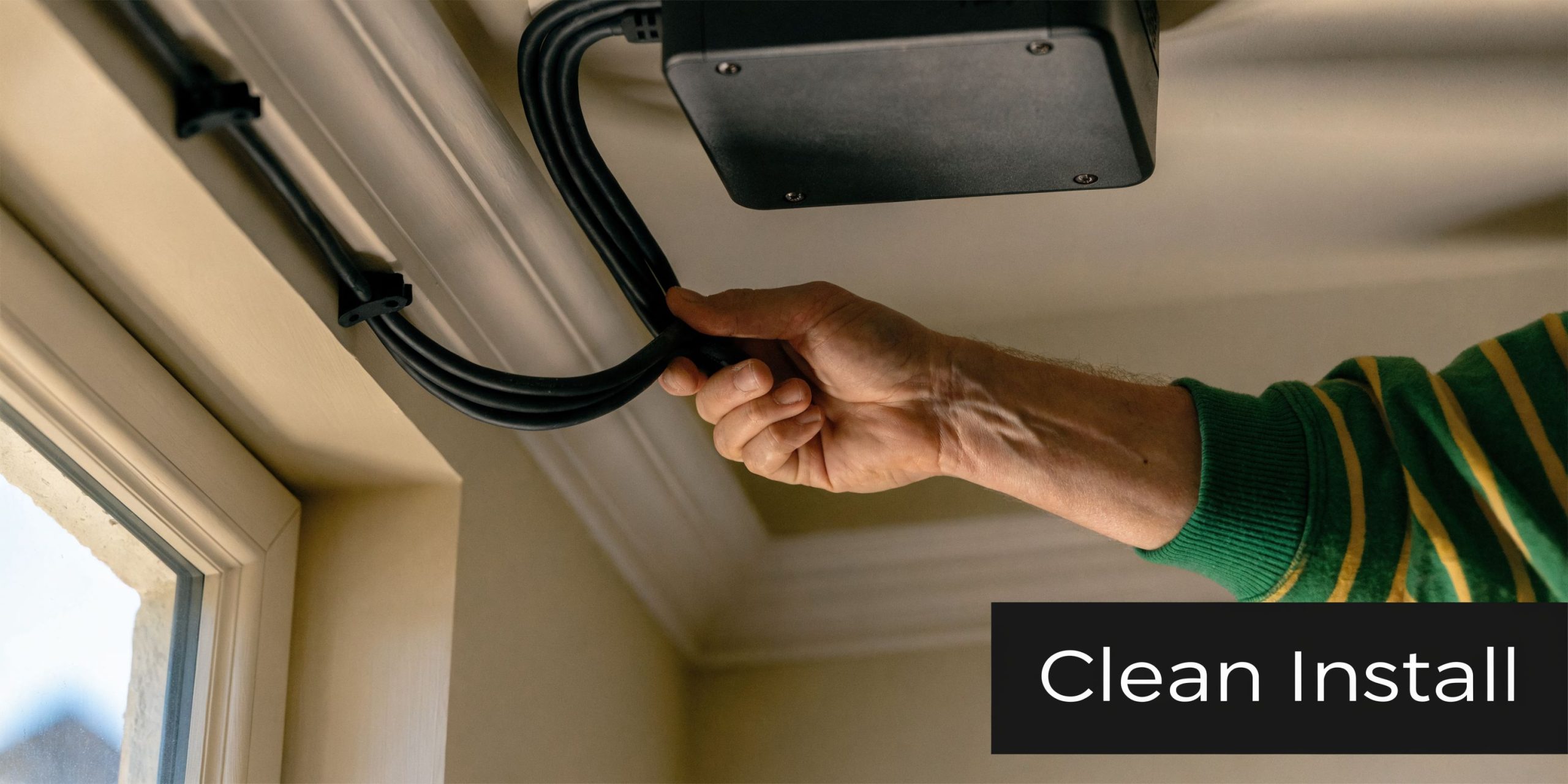 A person's hand neatly organizing black cables leading to a projector mounted on the ceiling