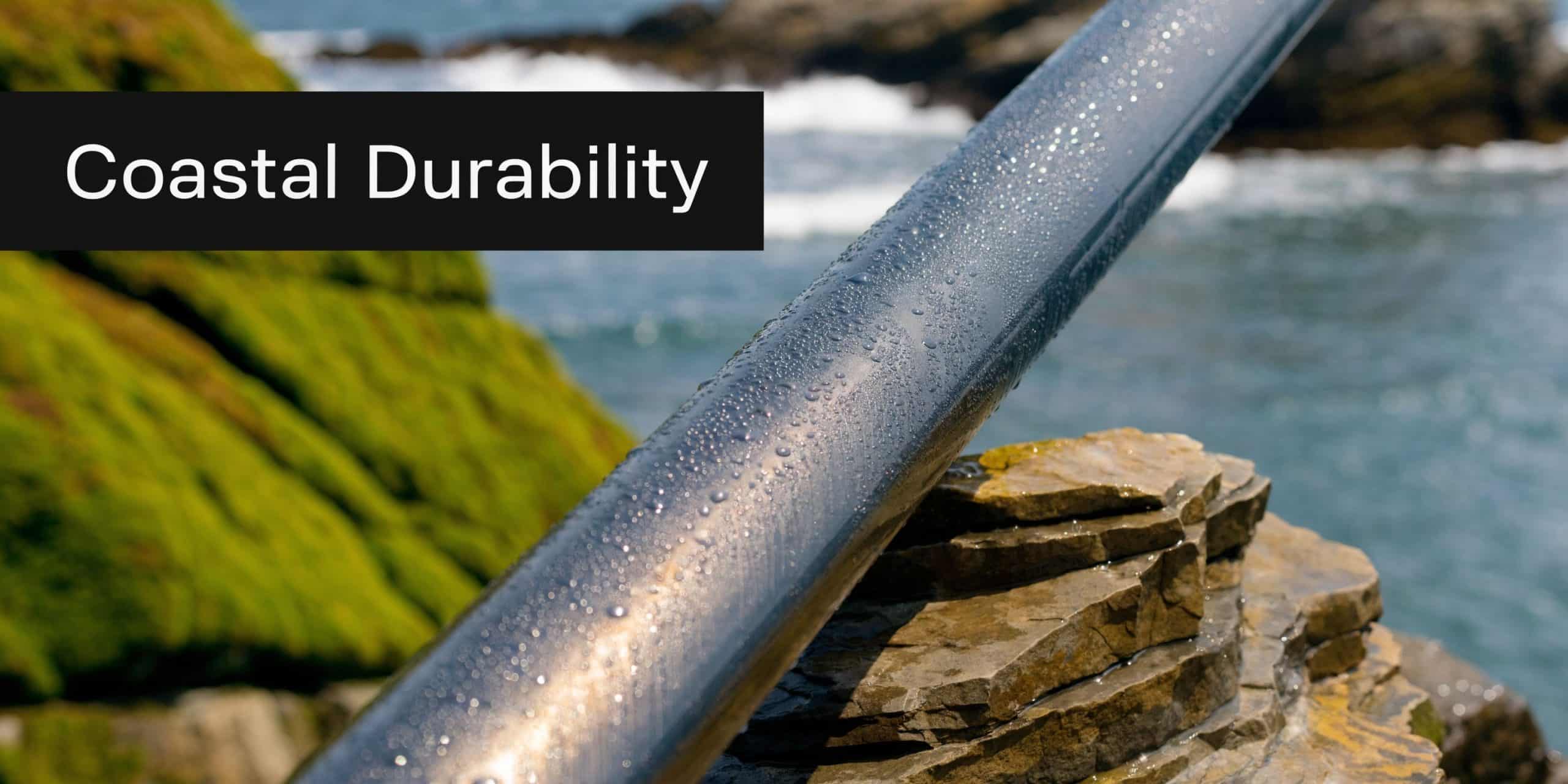 A smooth metal handrail covered in water droplets stands against a background of coastal rocks and sea.