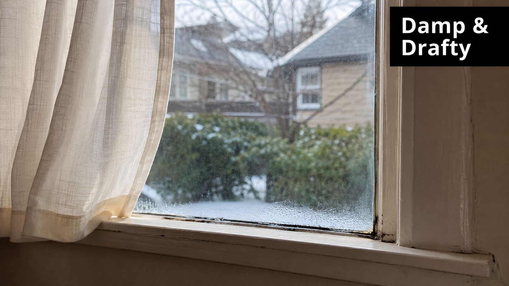 Condensation on an old drafty window with a white curtain overlooking a snowy winter yard